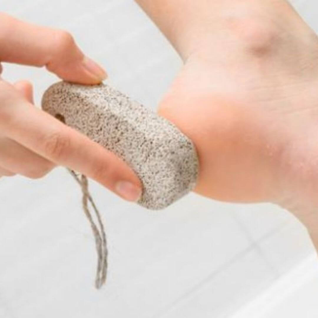 Uso de una piedra pómez para el cuidado de los pies en un entorno de baño.